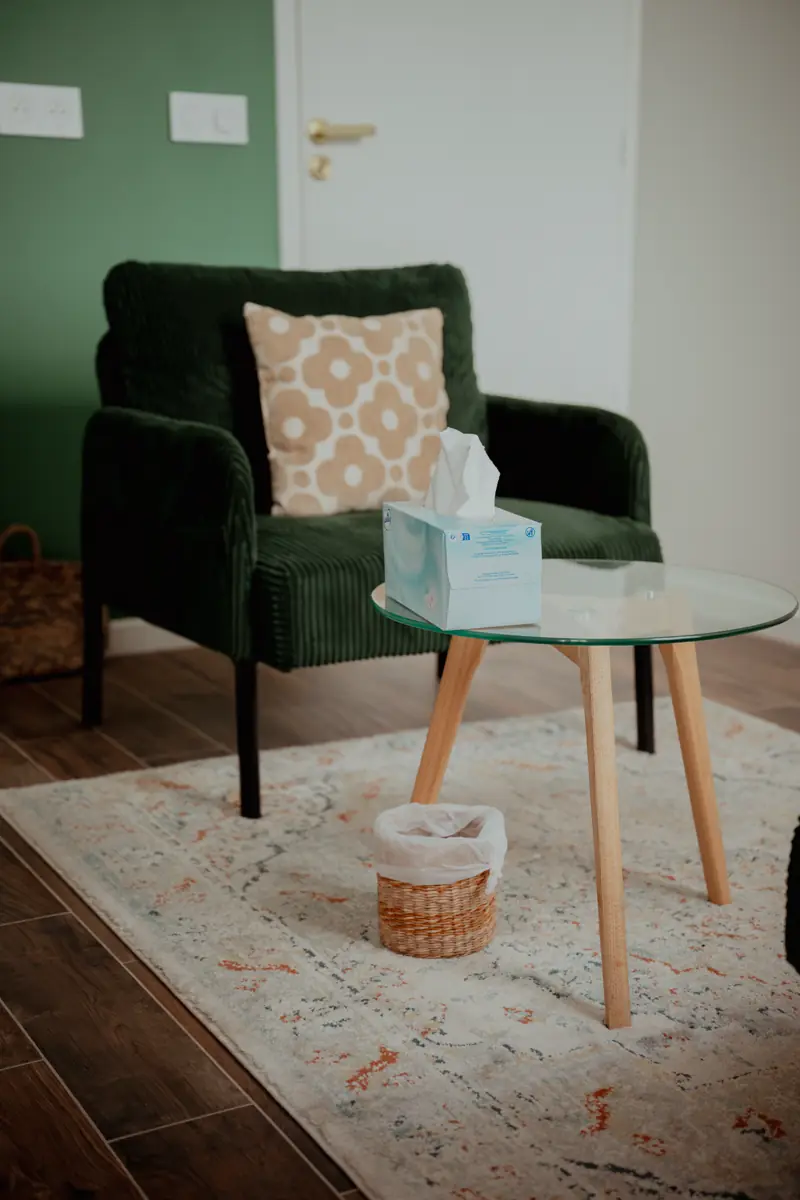 Un fauteuil en velours vert et un guéridon rond dans le cabinet, avec une boîte de mouchoirs.