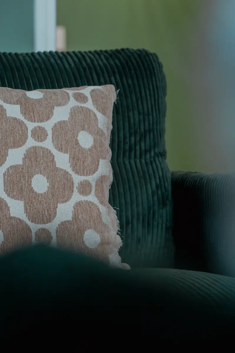 Un coussin à motifs fleuris posé sur un fauteuil en velours vert.