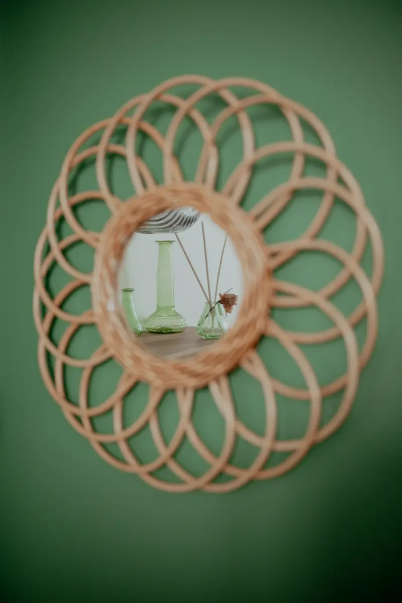 Un miroir en rotin en forme de rosace, accroché sur un mur vert du cabinet.